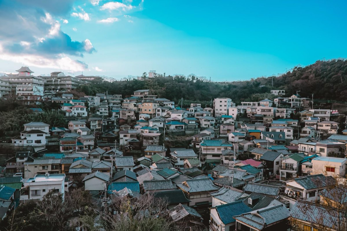 青い空の下、丘の斜面に瓦屋根や白い外壁の住宅がぎっしりと重なり合って並ぶ街の眺め